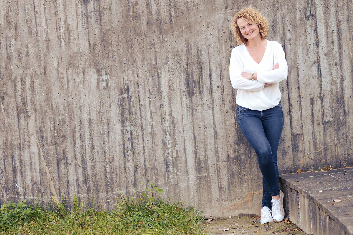 Alexandra Brindlinger sitzt an einem Tisch und spricht mit geöffneten Händen, als würde sie in einem ruhigen Gespräch Klarheit im Brandingprozess begleiten.